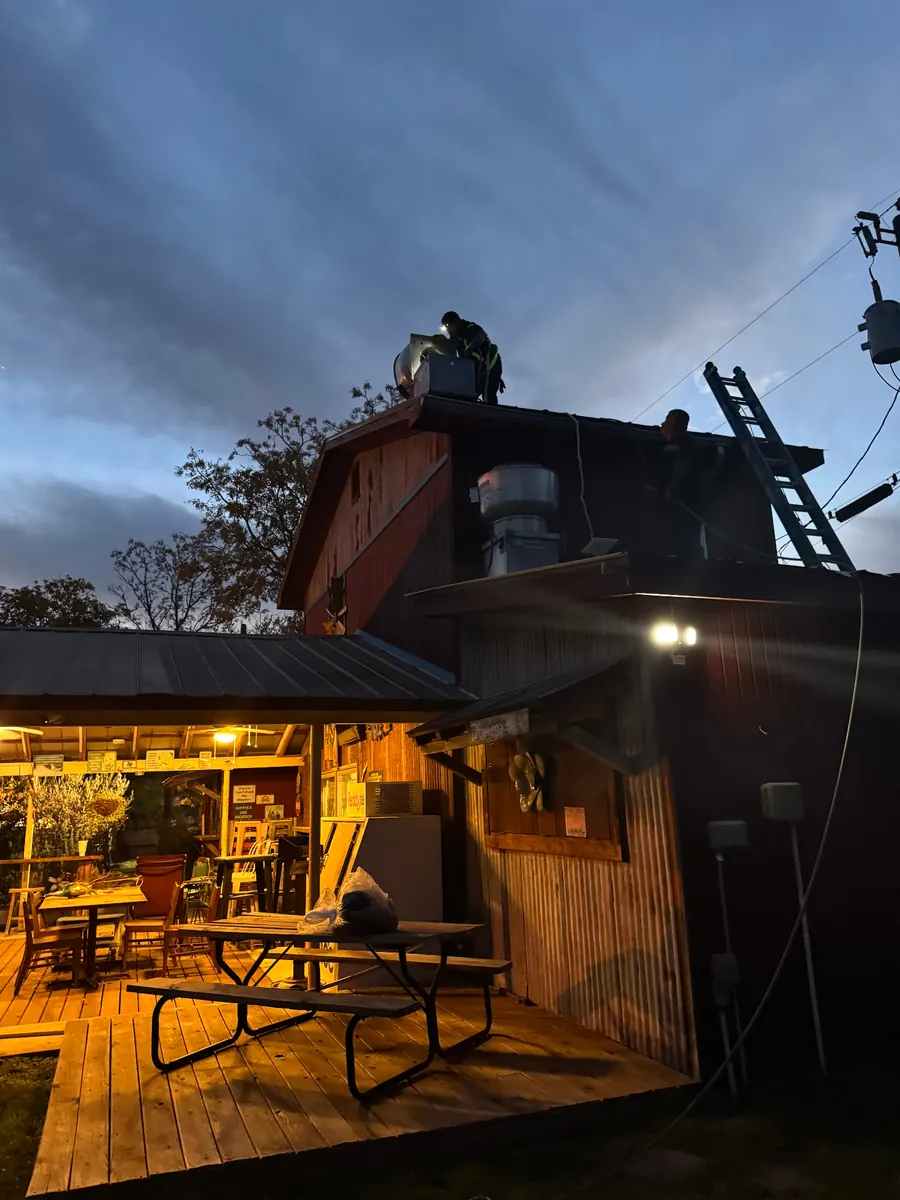 Crew servicing exhaust fan on barn-style restaurant at dusk