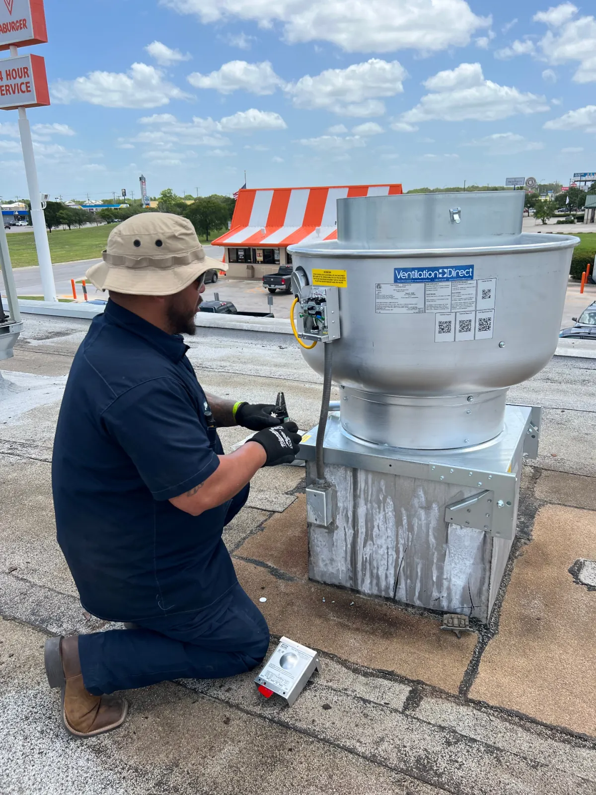 Technician servicing rooftop upblast exhaust fan on Texas restaurant roof