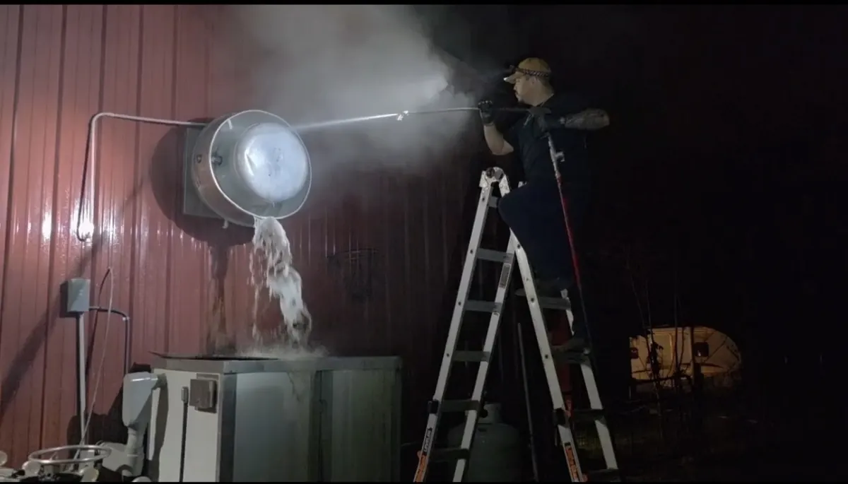 Technician on ladder hot-water washing exterior exhaust fan at night